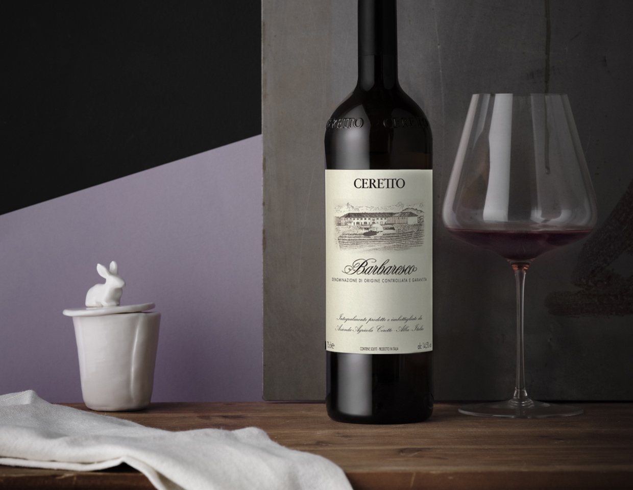 Bottle of Ceretto Barbaresco and glass of wine on wooden table in front of geometric wallpaper.