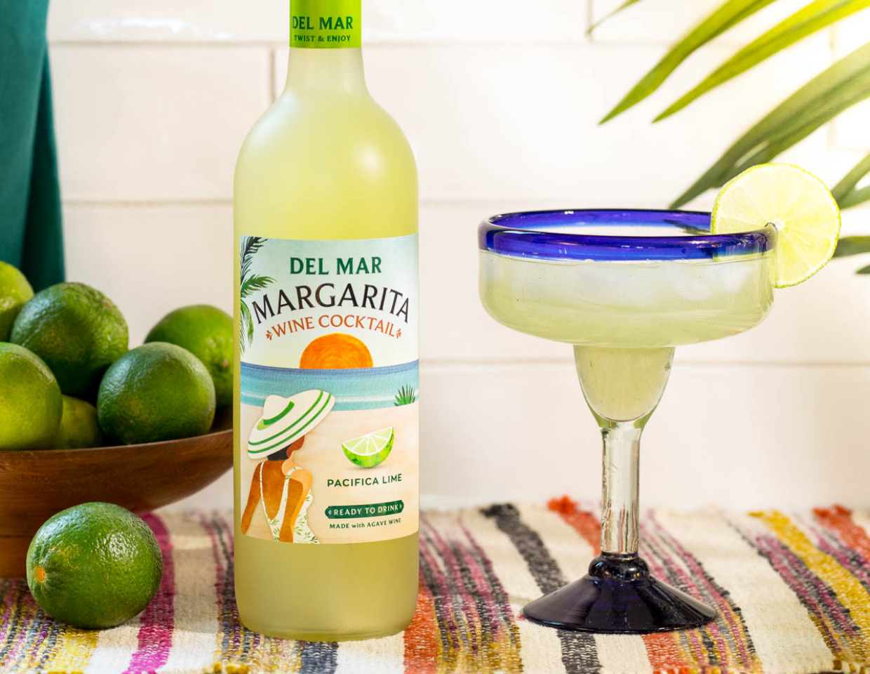Bottle of Del Mar margarita wine cocktail on a counter with limes next to a margarita glass.