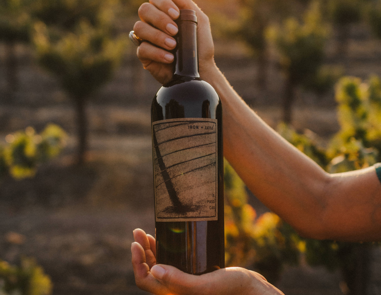 Woman holding bottle of Iron + Sand Cabernet Sauvignon in a beautiful sunlit winery