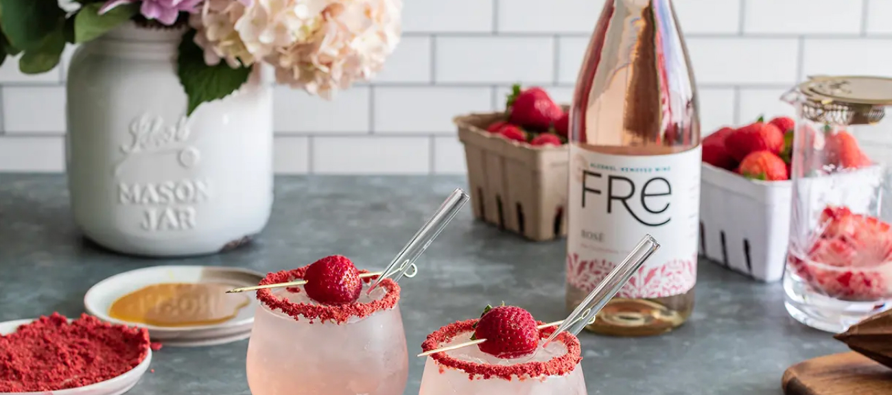 Bottle of FRE rose on a table with fresh strawberries and two bright-pink strawberry smash mocktails