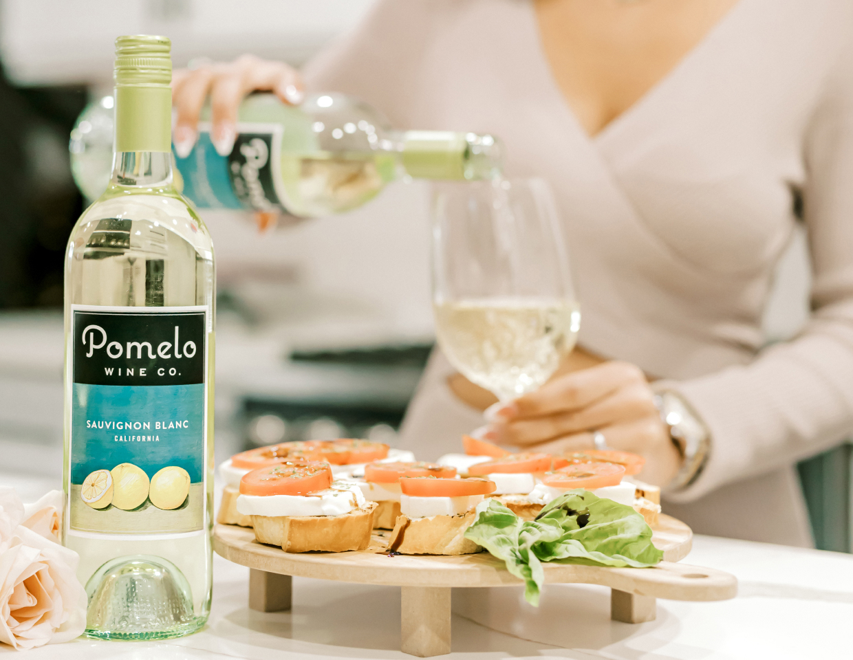 Woman pouring a glass of Pomelo Sauvignon Blanc next to a platter of appetizers.