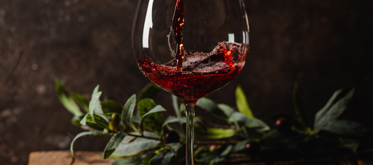 Red wine being poured into a large glass on a table with green leaves.
