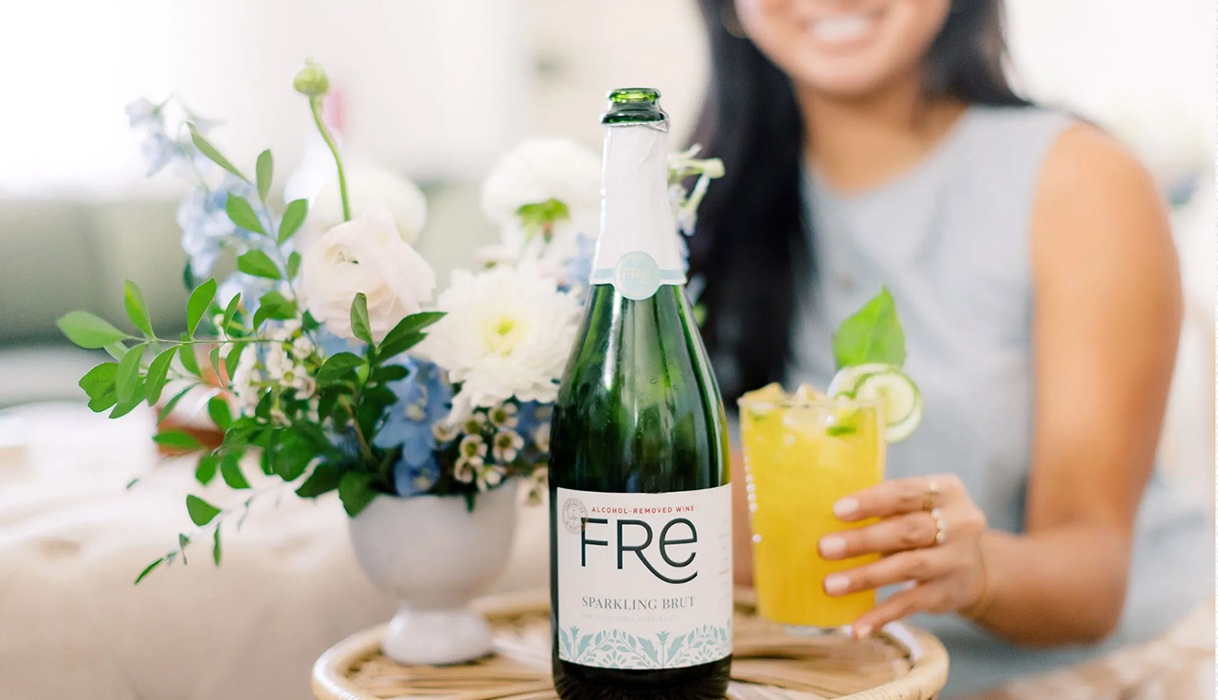 Woman holding a Cucumber basil citrus mocktail with a bottle of FRE Sparkling Brut and flowers