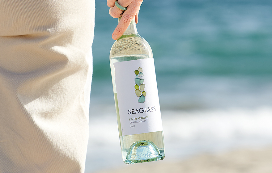 Person on the beach holding a bottle of SEAGLASS pinot grigio