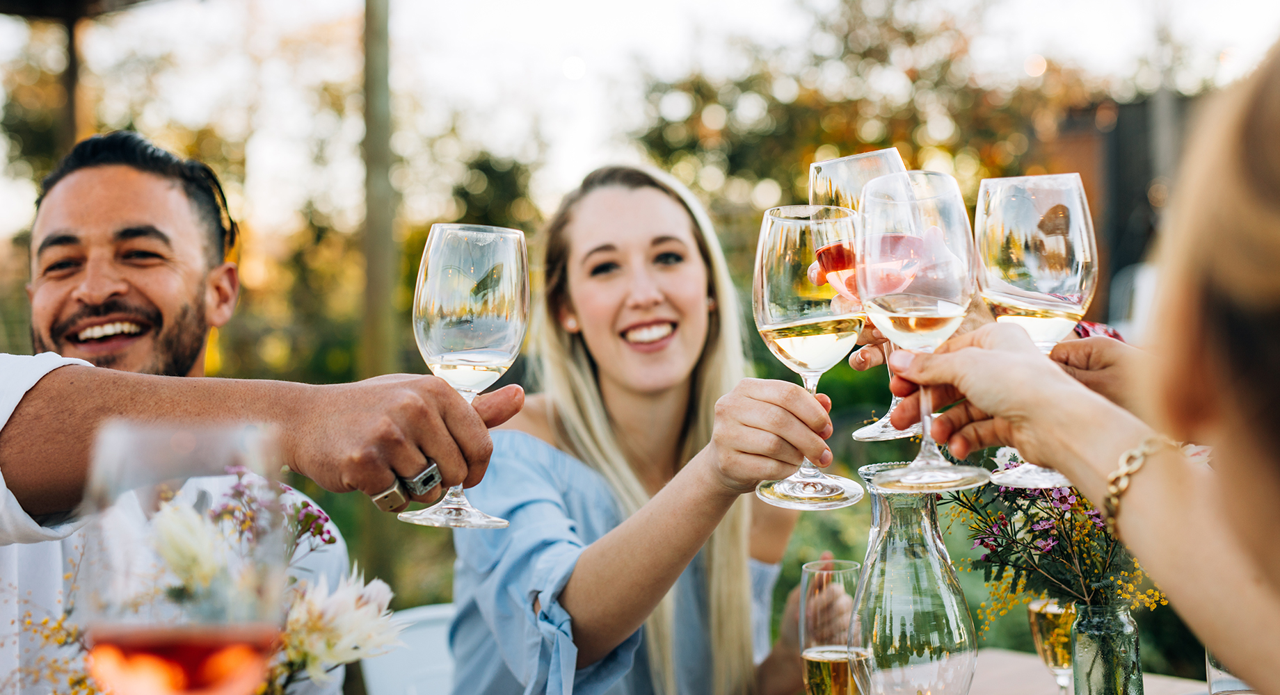 Group of friends dining outside in the summer and toasting with a glass of wine