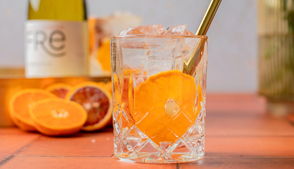 Citrus Breeze Chardonnay mocktail in a clear glass with FRE Chardonnay and orange slices in the background