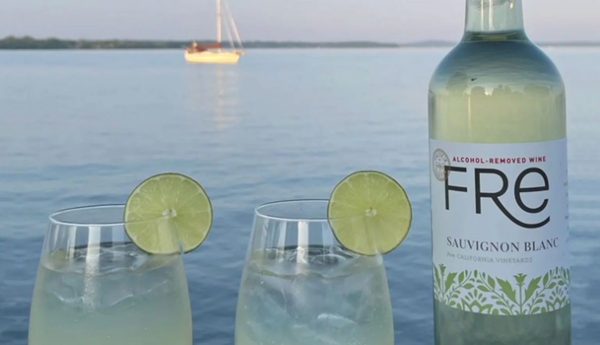 Margarita wine spritzer mocktails next to a bottle of FRE alcohol-removed sauvignon blanc with the sun setting over the ocean behind it