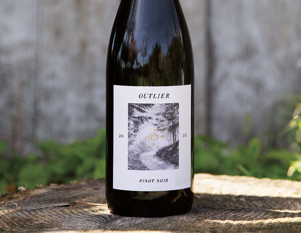 Bottle of Outlier pinot noir on an outdoor table with grass in the background
