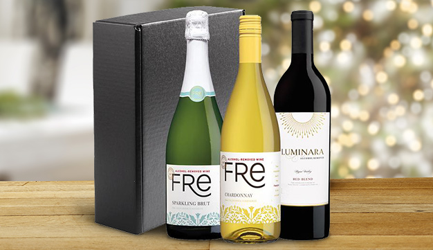 Alcohol-removed wine gift set with FRE sparkling brut, FRE chardonnay, and Luminara red blend on a table with a christmas tree in the background