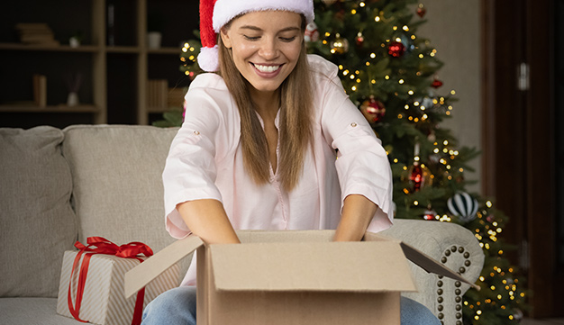 woman in a santa hat unboxing a shipment from one stop wine shop with a christmas tree behind her
