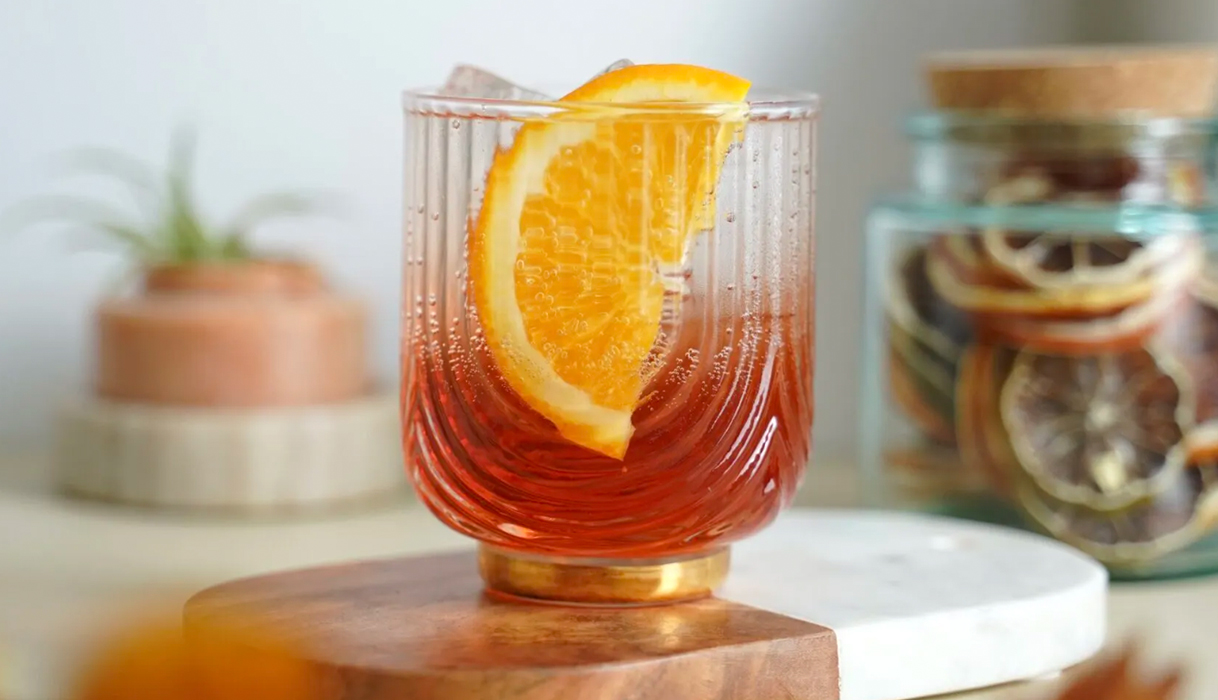 FRE bicicletta mocktail in a fancy rocks glass next to a jar of orange slices with a plant in the background
