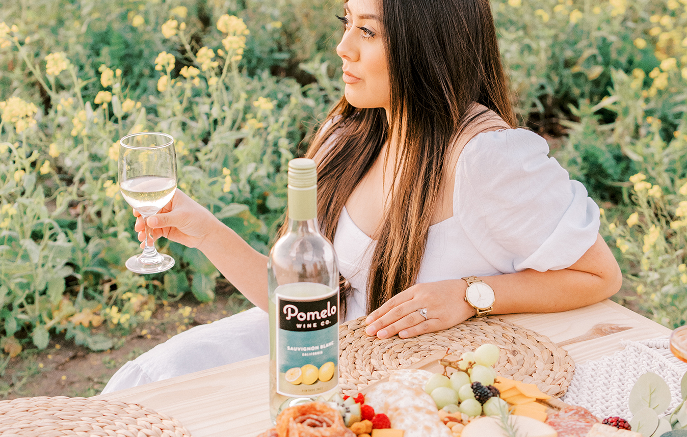woman enjoying a glass of pomelo sauvignon blanc at a picnic with lush greenery