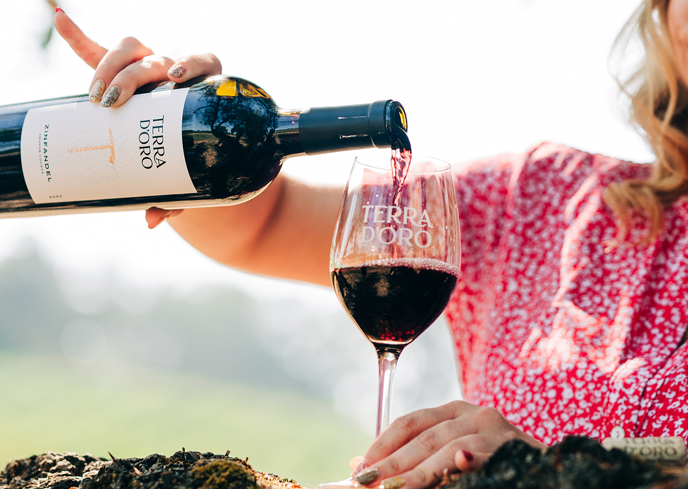 Woman pouring from a bottle of Terra d'Oro zinfandel into a glass outside on a tree branch