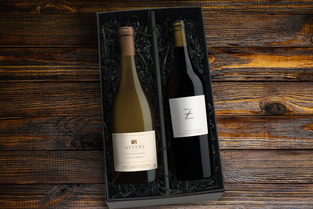 Bottles of Neyers carnernos chardonnay and ZIATA cabernet sauvignon in a black gift box on a dark wood surface