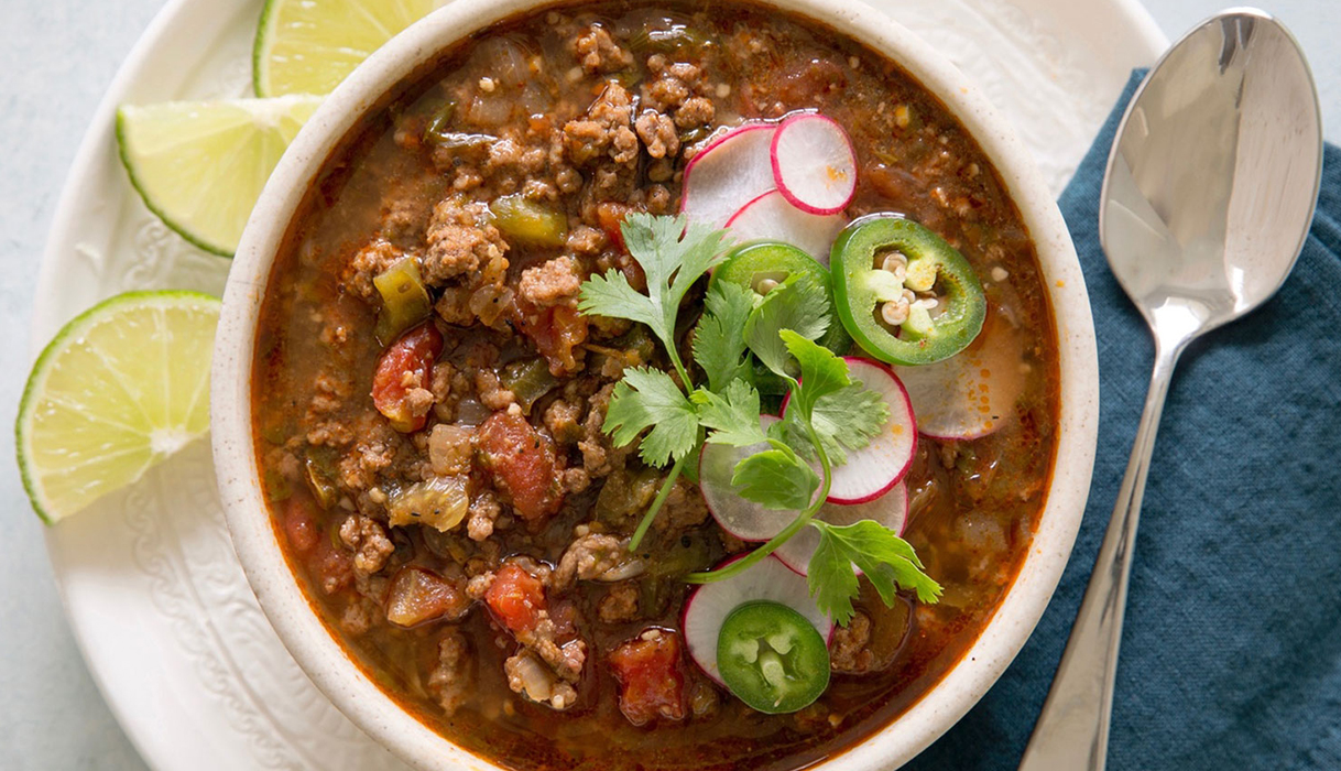 Bowl of vegetarian chili verde topped with sliced jalapeños with a spoon and napkin nearby.