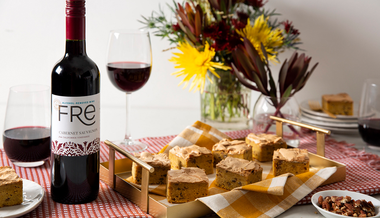 bottle and two glasses of FRE alcohol-removed cabernet sauvignon next to a tray of pumpkin chai brownies with a vase of fall flowers in the background