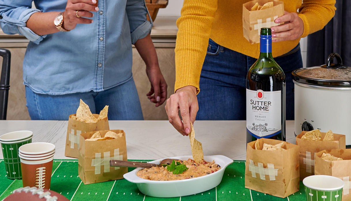 two women enjoying cheesy sausage dip with tortilla chips and Sutter Home merlot on a football game day