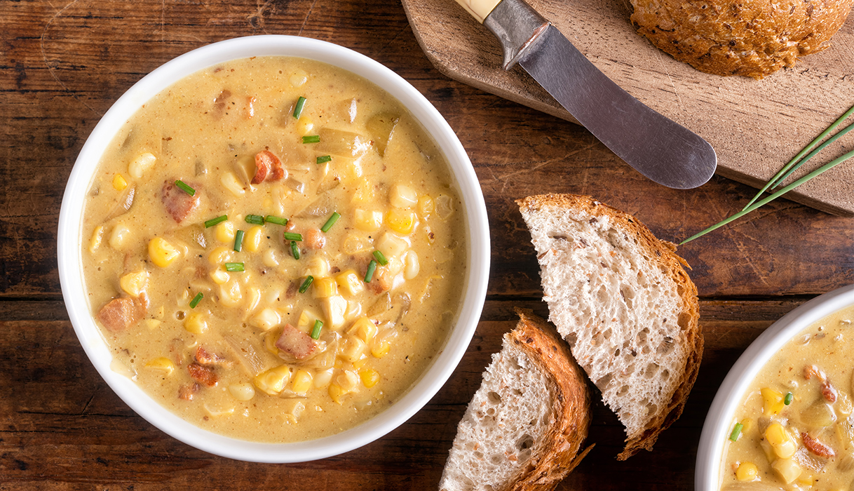 bowl of bacon corn chowder next to freshly sliced bread