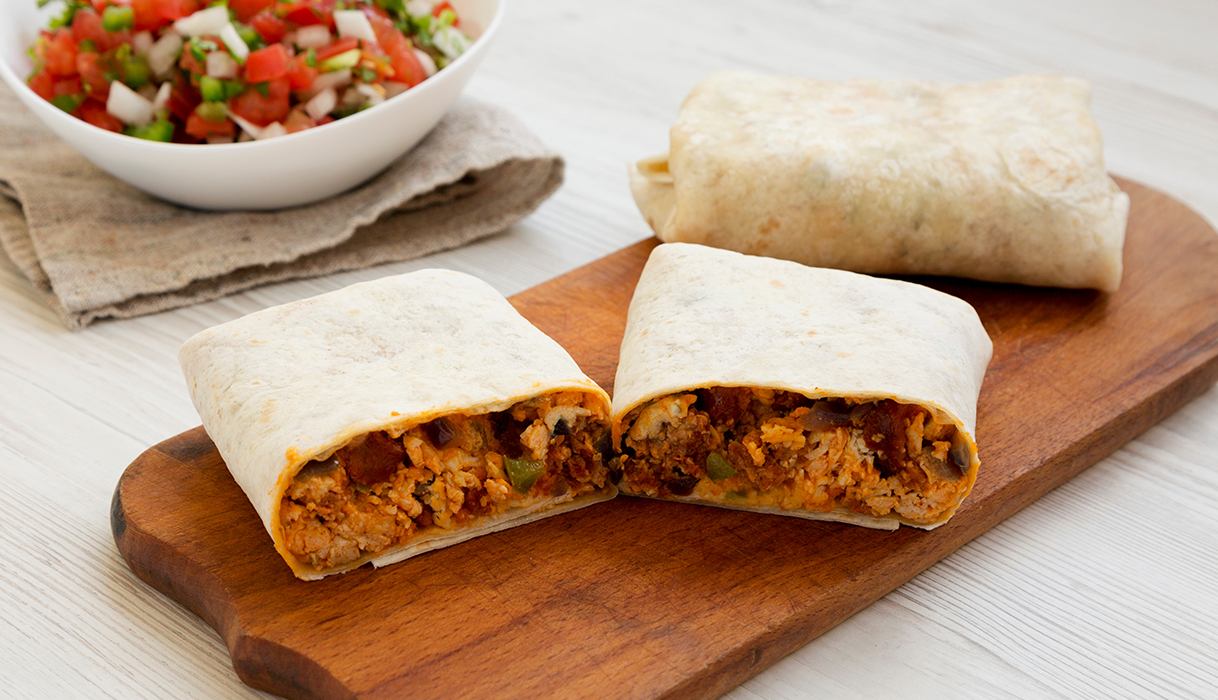 chorizo burrito cut in half on a cutting board with a bowl of salsa in the background.