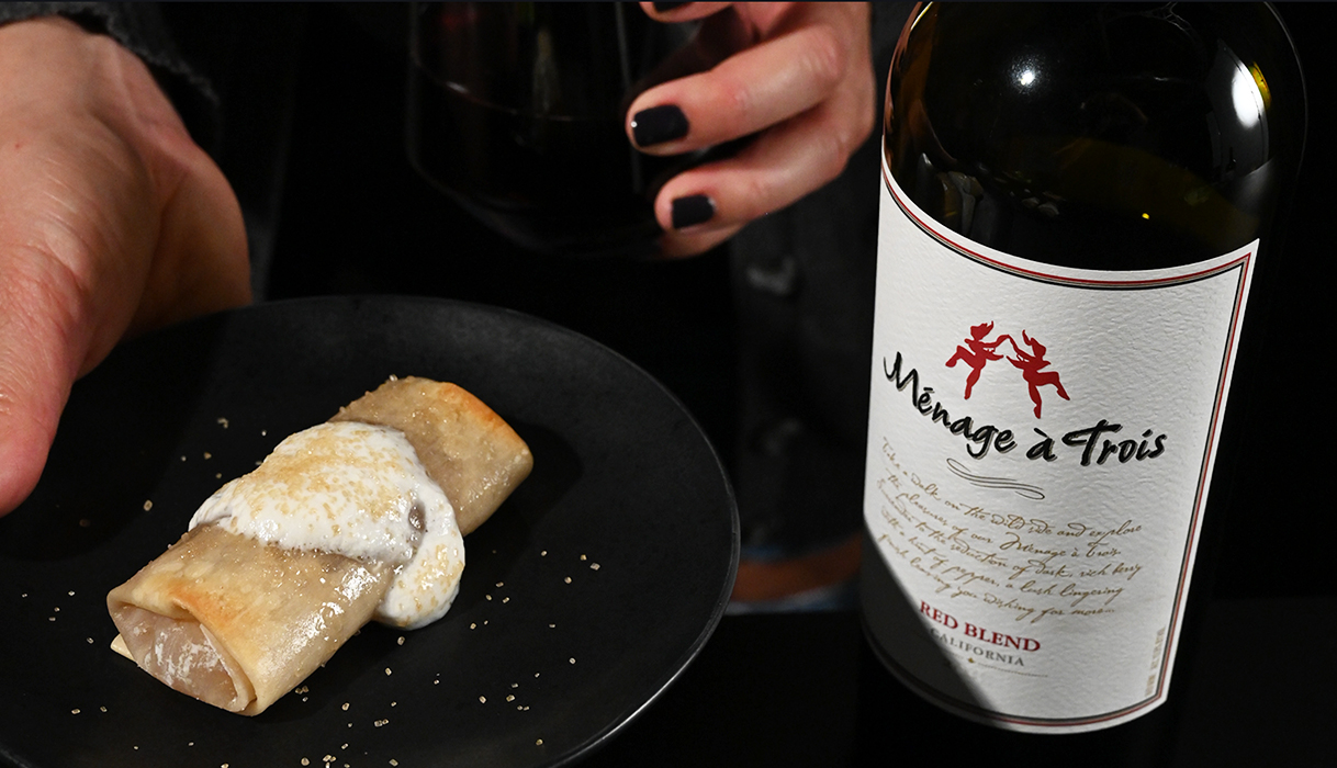 Apple eggroll on a plate with whipped cream on top next to a bottle of Menage a Trois red blend