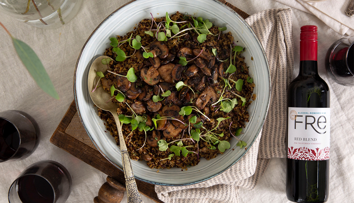 A bowl of Portobello Quinoa Risotto with microgreens on top, next to a bottle and three glasses of FRE alcohol-removed red blend.