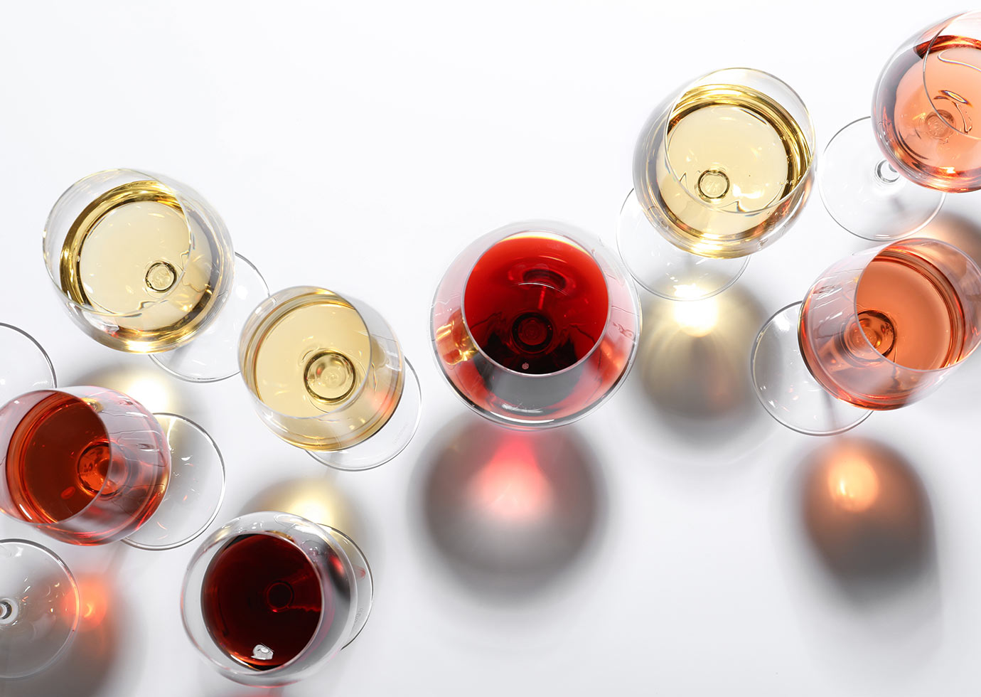 various glasses of different wines shown from above on a white background