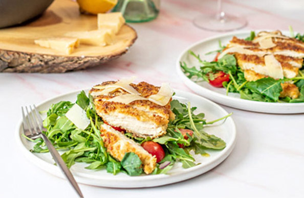 two white plates of panko chicken salad topped with fresh parmesan cheese.