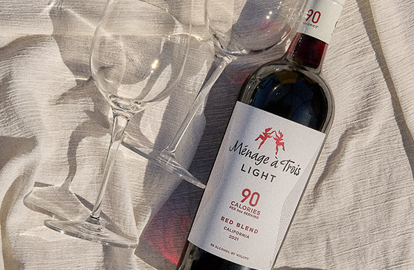 bottle of newly released menage a trois light red blend on a white tablecloth next to wine glasses