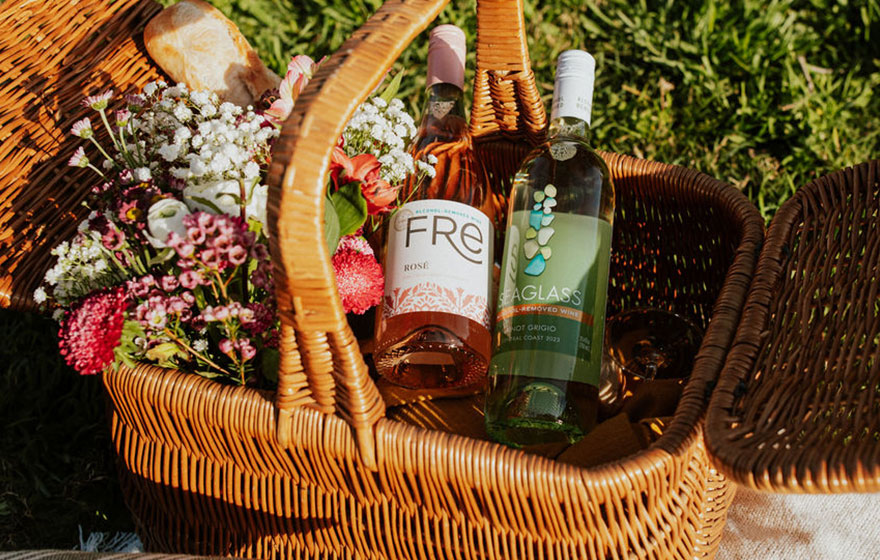 a bottle of fre alcohol-removed rose and seaglass alcohol removed pinot grigio in a picnic basket with a bouquet of spring flowers