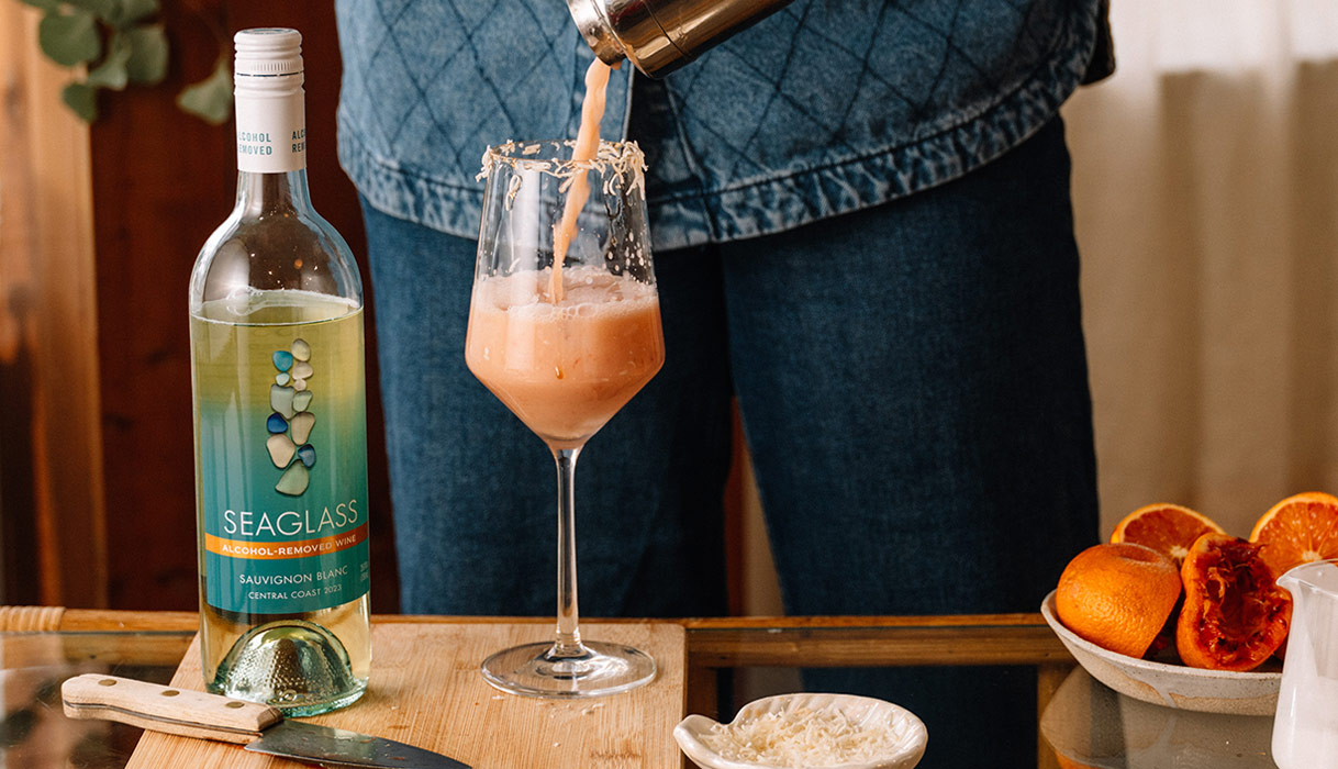 person mixing up a coconut blood orange mocktail made with SEAGLASS alcohol-removed sauvignon blanc