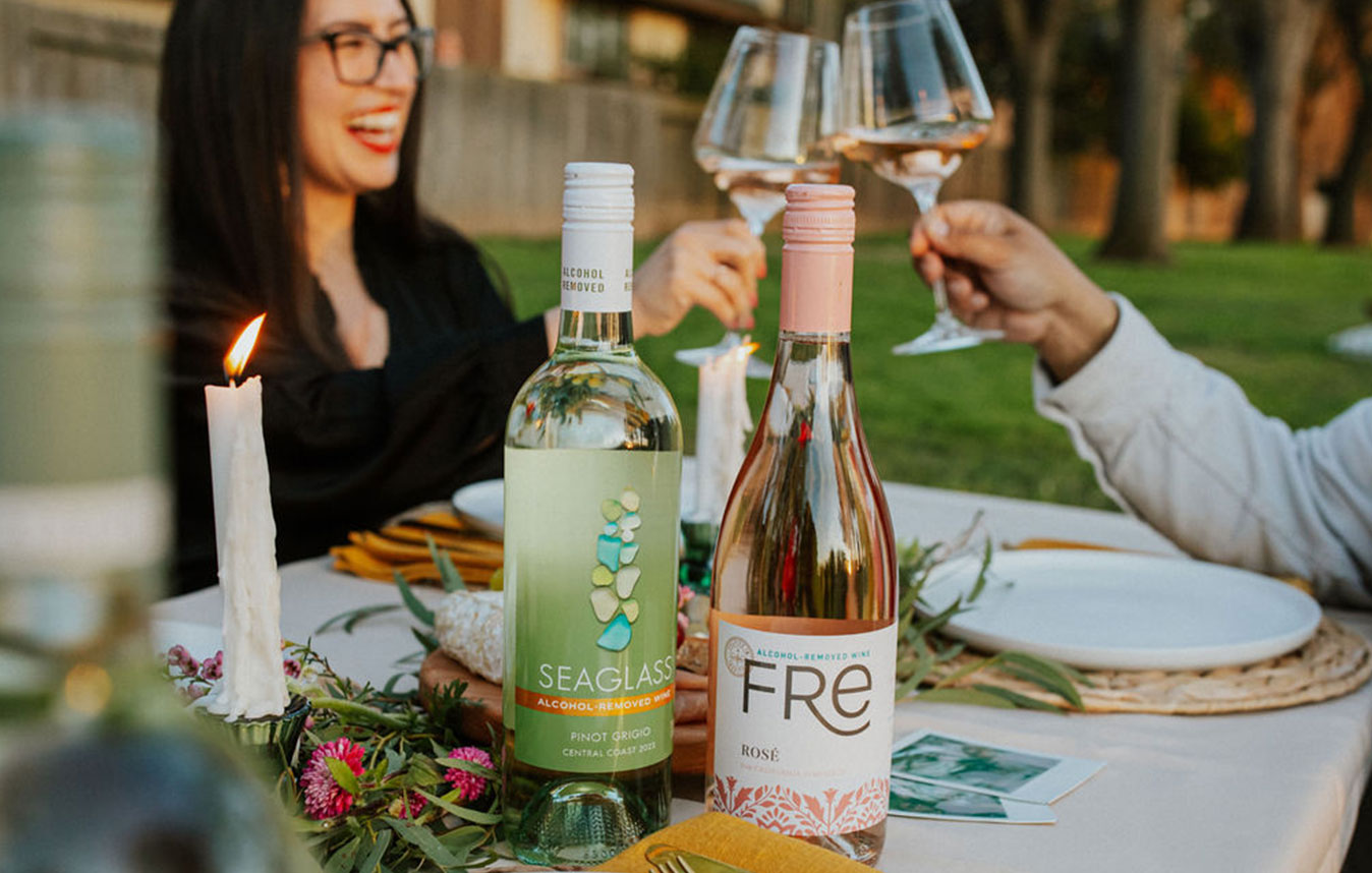 two people at an outdoor dinner party clinking glasses of premium alcohol-removed wines like SEAGLASS alcohol-removed pinot grigio and FRE alcohol-removed rose.