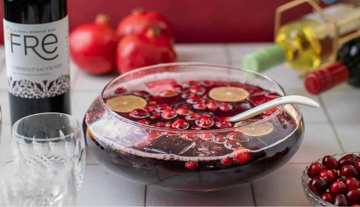 A bowl of festive holiday punch with floating cranberries and lime slices featuring FRE alcohol-removed cabernet sauvignon. Get this recipe and more mocktail recipes at One Stop Wine Shop.