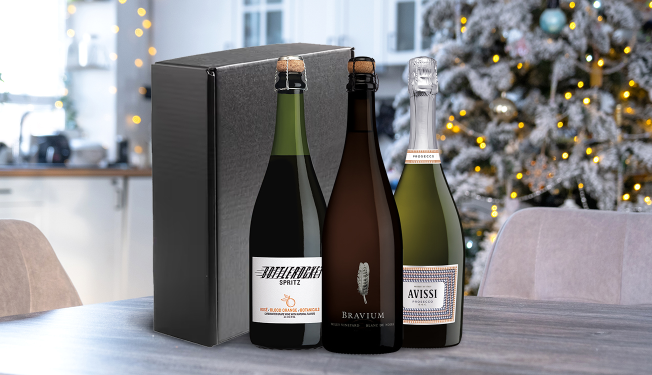 A sparkling trio gift set from One Stop Wine Shop on a dining room table with a decorated tree in the background. Shop this and more wine gift sets.