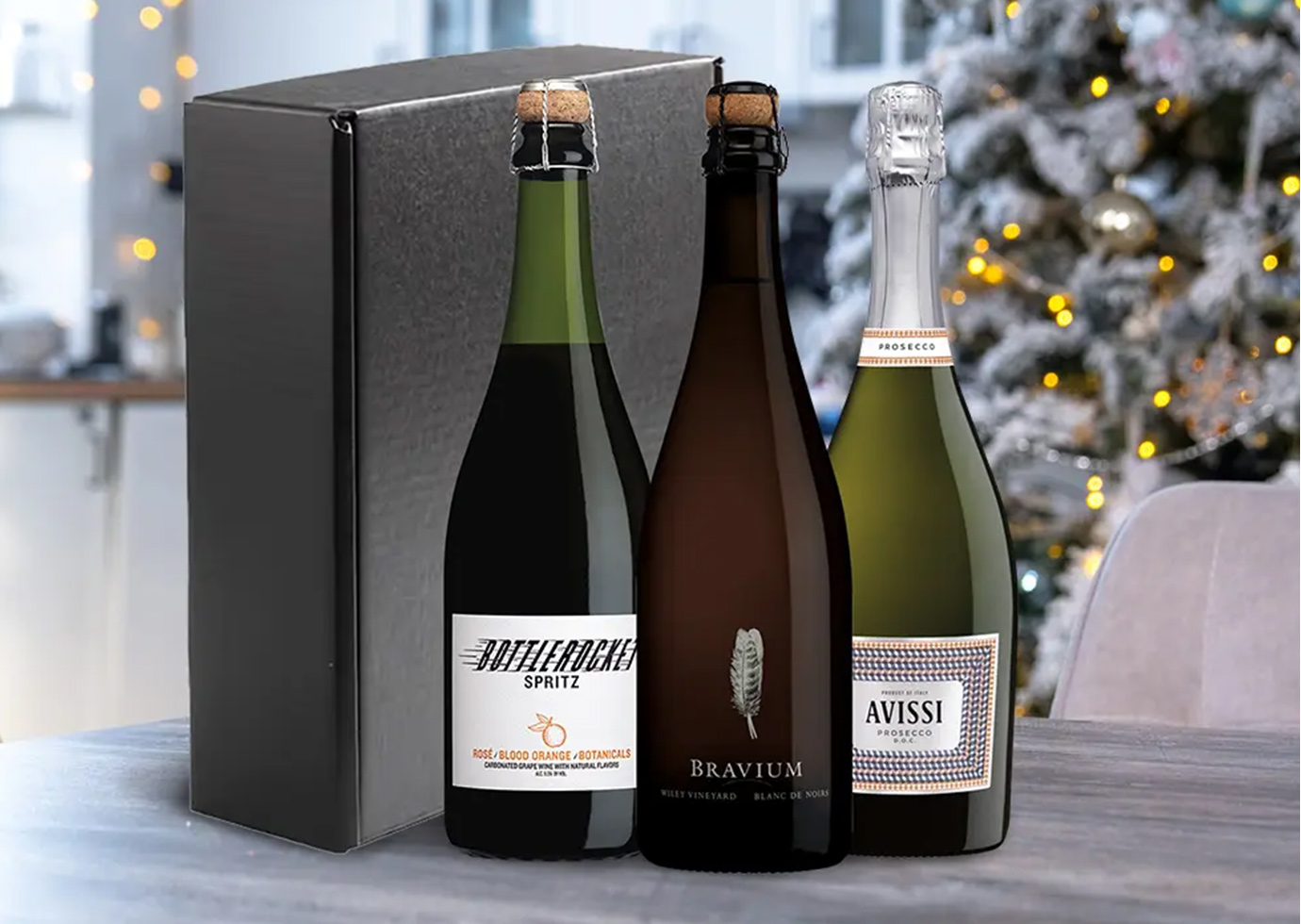 A sparkling trio gift set from One Stop Wine Shop on a kitchen table with a white Christmas tree in the background. Buy this and more holiday gift sets only at One Stop Wine Shop.