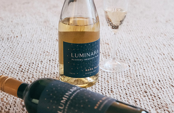 A bottle and glass luminara sparkling alcohol-removed wine on a white carpet with a bottle of Luminara cabernet sauvignon alcohol removed wine laying down in front of it. Shop these alcohol-removed wines and more at One Stop Wine Shop
