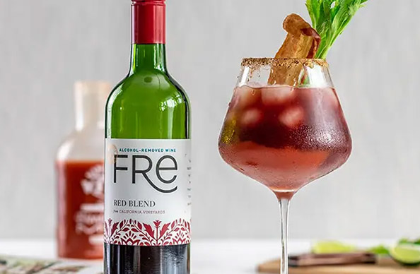A bottle of FRE alcohol-removed red blend next to a virgin bloody Mary garnished with a slice of bacon and celery stick. Get this mocktail recipe and more at One Stop Wine Shop.