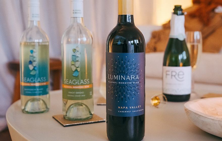 various bottles of alcohol removed wines on a table in front of a cozy couch. Shop the large selection of alcohol-removed wines only from One Stop Wine Shop