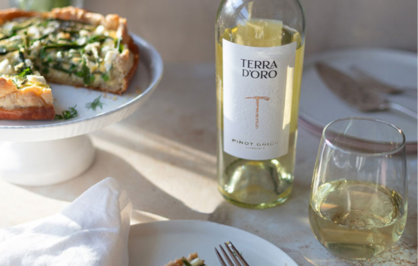 A bottle and glass of Terra d'Oro pinot grigio next to a spring quiche on a cake stand.