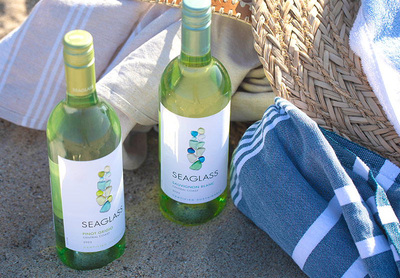 a bottle of SEAGLASS pinot grigio and sauvignon blanc on the beach surrounded by beach blankets