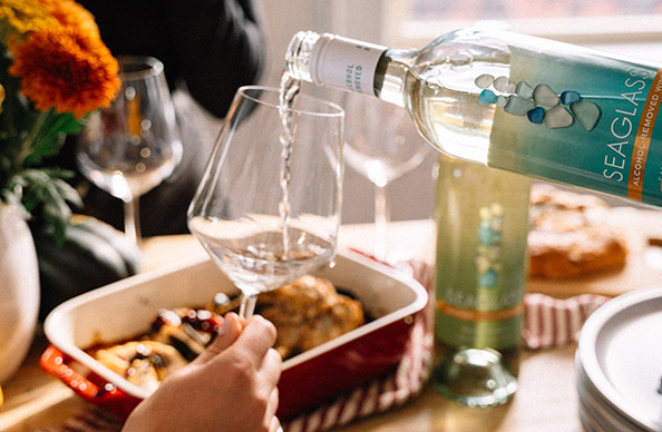 Person pouring a glass of SEAGLASS alcohol-removed sauvignon blanc in front a table set for a fall brunch