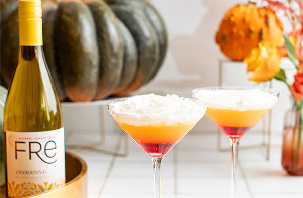 A bottle of FRE alcohol-removed chardonnay next to two glasses of candy corn fauxtinis, a layered mocktail ready for Halloween