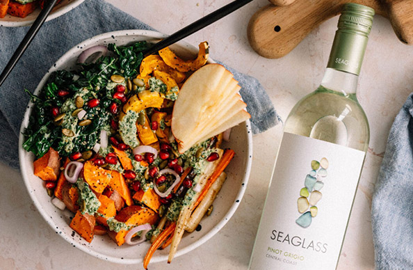 A harvest bowl full of brightly colored fall vegetables next to a bottle of SEAGLASS pinot grigio