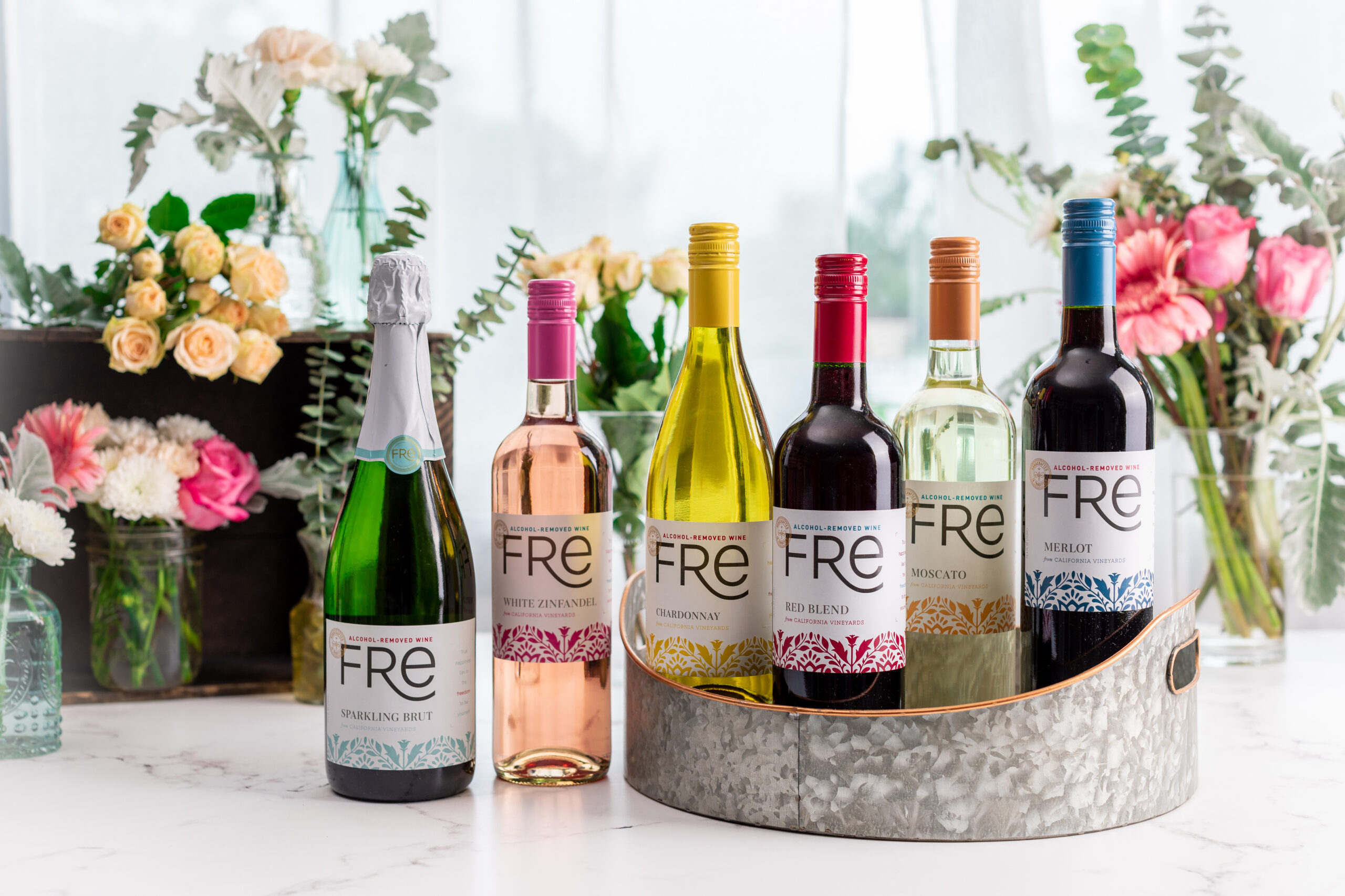 A selection of six bottles of Fre non-alcoholic wine with a display of flowers in the background