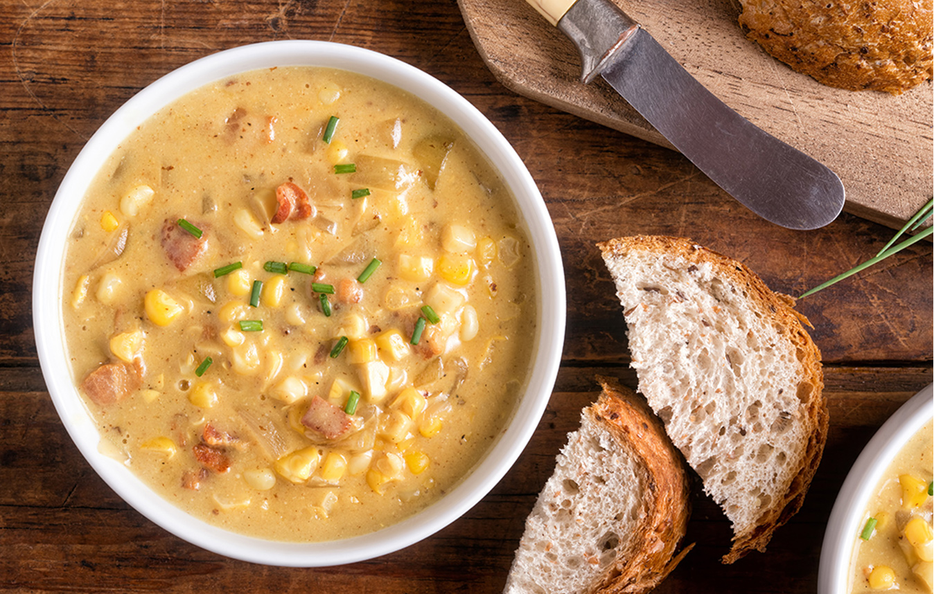 A bowl of bacon corn chowder next to freshly sliced bread