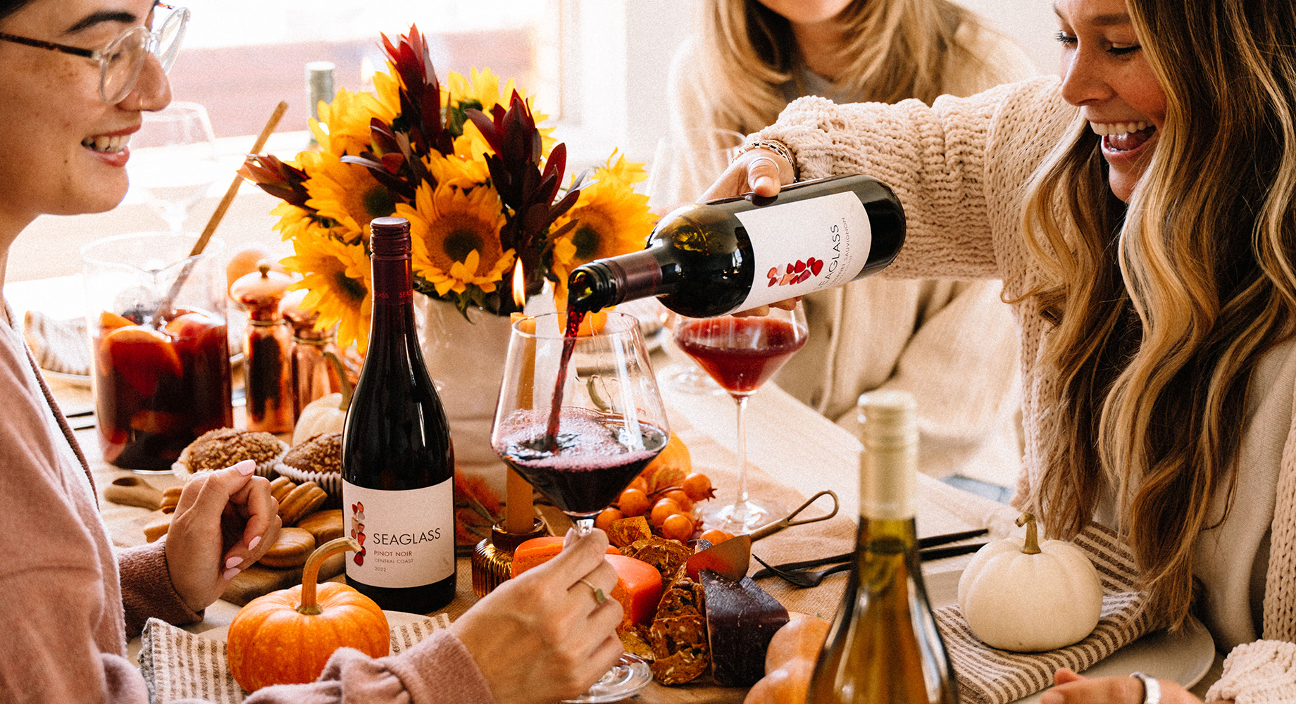 Three woman enjoying glasses of SEAGLASS wines during a fall dinner at a table set with pumpkins.